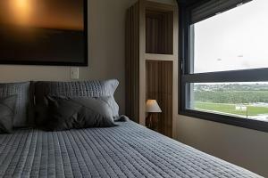 a bedroom with a bed with a large window at Studio 907 Flow Live - Parque Una + garagem in Pelotas