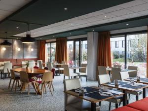 a dining room with tables and chairs and windows at ibis Lyon Est Meyzieu in Meyzieu