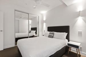 a white bedroom with a large bed and a mirror at District Apartments Fitzroy in Melbourne