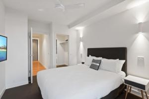 a white bedroom with a large bed and a table at District Apartments Fitzroy in Melbourne