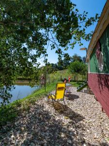 a yellow chair sitting next to a building next to a lake at Ecrin du Ségala - Roulotte insolite in Tauriac-de-Naucelle