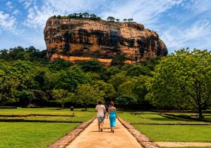 two people walking down a path in front of a mountain at Wihara Cottage Sigiriya in Sigiriya