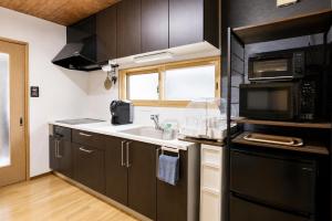 a kitchen with black cabinets and a sink and a microwave at Chillax Hida Takayama in Takayama