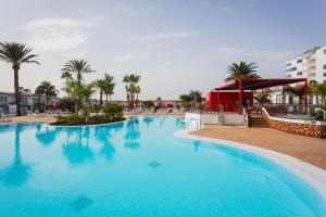 a large blue swimming pool with palm trees and a building at Sholeo Lodges Maspalomas in Playa del Ingles