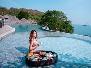 a woman sitting next to a pool with a tray of food at Novotel Koh Si Chang in Ban Phanu Rangsi