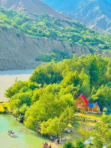 a house on the shore of a river next to a mountain at Fish Lake Park Guest House in Chitral