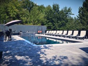 a swimming pool with benches and an umbrella at Kuća za odmor Đogić - bazen & jacuzzi in Ilidža