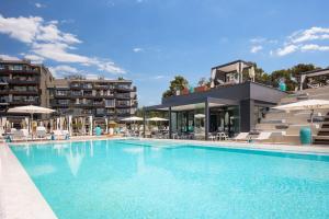 a swimming pool with chairs and umbrellas next to a hotel at Aminess Younique Vollo Hotel Residences in Opatija