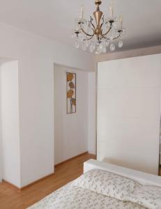 a white bedroom with a bed and a chandelier at Brasov Sfat Apartament in Braşov