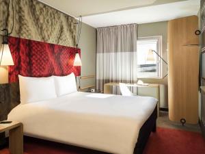 a hotel room with a large white bed with a red blanket at ibis Paris Saint-Denis Stade Sud in Saint-Denis +41 photos