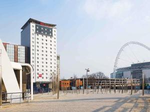 a tall white building with a ferris wheel in the background at ibis London Wembley in London