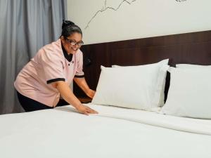 a woman making a bed in a bedroom at Mercure Jaragua do Sul in Jaraguá do Sul