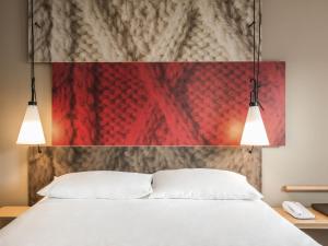 a bedroom with a white bed and two lights at Ibis Aéroport Bâle Mulhouse in Saint-Louis