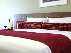 a large bed with red and white sheets and pillows at Mercure Sydney Liverpool in Liverpool