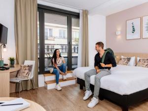 a man and woman sitting on beds in a hotel room at Aparthotel Adagio Access Bruxelles Europe Aparthotel in Brussels
