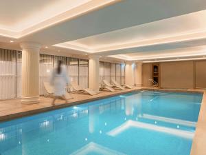 a woman walks past a swimming pool in a hotel at The Playford Adelaide - MGallery in Adelaide