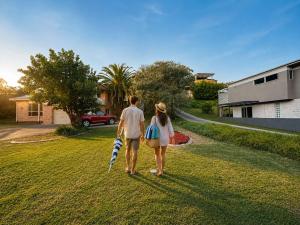 a man and woman walking down a yard with an umbrella at Palacete Beach - Resort Style Stay in Culburra Beach