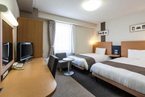 a hotel room with two beds and a desk with a tv at Comfort Hotel Shin Yamaguchi in Yamaguchi