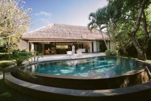 a woman standing next to a swimming pool in front of a house at Akilea Villas Bali in Uluwatu