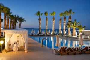 a resort with a pool with palm trees and chairs at Vrissiana Boutique Beach Hotel in Protaras