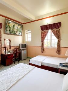 a bedroom with two beds and a desk and a window at Khách sạn Nam Sơn in Ấp Lợi Ðủ