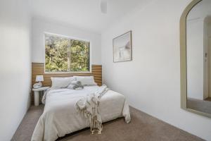 a white bedroom with a bed and a mirror at Relax at Flynn s View in Port Macquarie