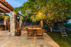 a patio with a table and chairs under a tree at Petalidi Olive Garden Stone House near the beach in Petalidi