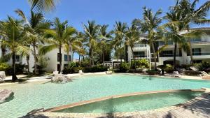 a large swimming pool with palm trees and a building at Experience the Pool View Dream at Estrella Dominicus in Bayahibe