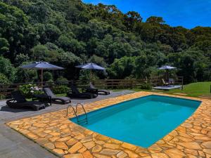 a swimming pool with chairs and umbrellas in a yard at Pousada Olivier da Montanha in Santo Antônio do Pinhal