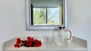 a mirror above a sink with red flowers and a vase at Experience the Pool View Dream at Estrella Dominicus in Bayahibe