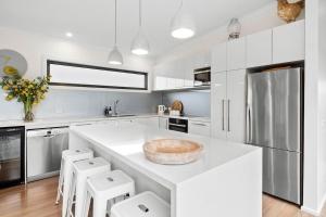 a white kitchen with a large island with stools at BYO Linen - Aireys Delight in Aireys Inlet +8 photos