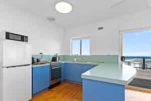 a kitchen with blue cabinets and a white refrigerator at Blue Surf - BYO Linen in Apollo Bay