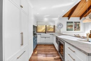 a kitchen with white cabinets and a wooden floor at Fern House in Lorne