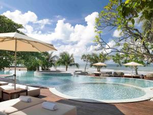 a swimming pool with chairs and umbrellas next to the ocean at Mercure Rayong Lomtalay Villas & Resort in Mae Pim