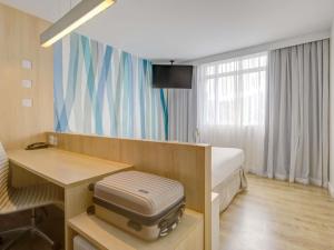 a room with a bed and a desk with a suitcase at Mercure Rio de Janeiro Barra da Tijuca in Rio de Janeiro