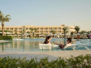 two people sitting in chairs in the swimming pool at a resort at Sofitel Ras Al Khaimah Al Hamra Beach Resort in Ras al Khaimah