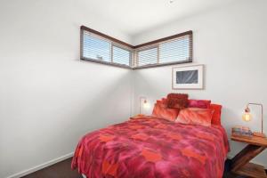 a bedroom with a bed with a red comforter and a window at Aireys Oasis in Aireys Inlet