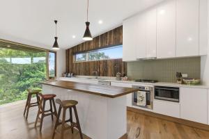 a kitchen with white cabinets and bar stools at Clovelly - BYO Linen in Lorne