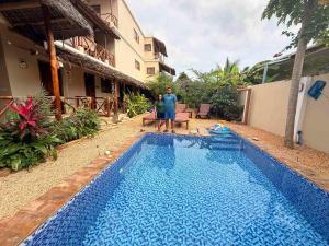a man standing next to a swimming pool next to a building at Peace And Color Limited Guest House in Nungwi