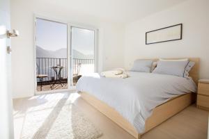 a white bedroom with a bed and a large window at Argegno Pool apartment by Italian Apartments in Argegno