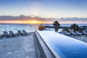 a swimming pool with chairs and the ocean at sunset at Barceló Teguise Beach - Adults Only in Costa Teguise