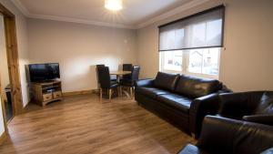 a living room with a leather couch and a television at Morris Gardens Apartments in Oldmeldrum