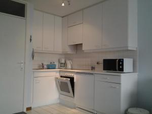 a white kitchen with white cabinets and a microwave at Zonnig Appartement met Zeezicht in Koksijde