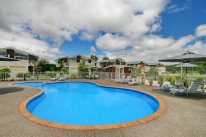 a pool at a resort with chairs and an umbrella at Oceans Resort Whitianga in Whitianga