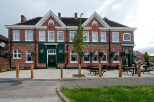 un gran edificio de ladrillo con bancos delante en The Greenwood Hotel - Wetherspoon en Northolt