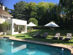 a swimming pool with two umbrellas and chairs next to a house at Chambery in Cape Town