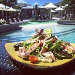 a salad on a yellow plate next to a swimming pool at 1770 Lagoons Central Apartment Resort in Agnes Water