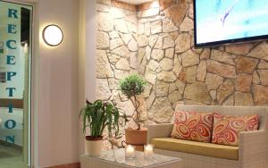 a living room with a couch and a tv on a stone wall at Amaryllis Hotel Apartments in Tolo