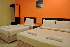 Zwei Betten in einem Hotelzimmer mit orangefarbenen Wänden in der Unterkunft Wau Hotel & Cafe in Jerantut