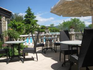 un patio con mesas, sillas y una sombrilla en Logis Hôtel Le Vieil Amandier en Trigance